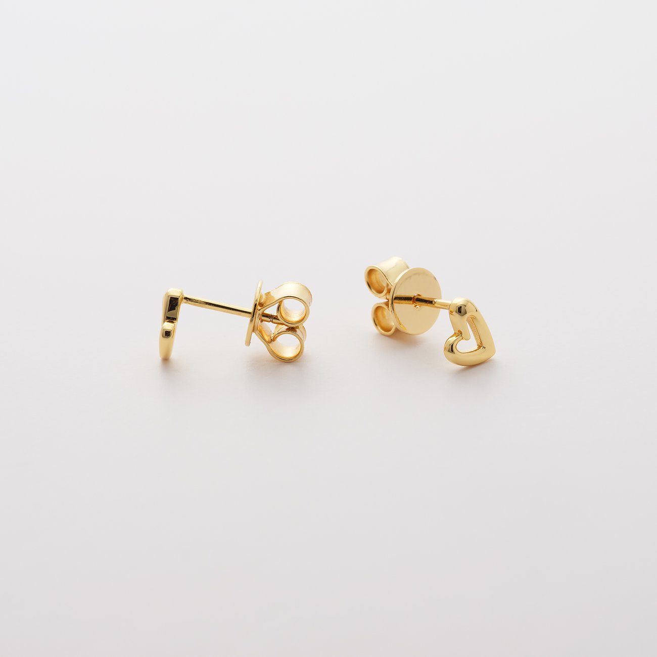 Zwei goldene JETTE Ohrstecker aus recyceltem 925er Silber in Herzform liegen leicht versetzt nebeneinander.