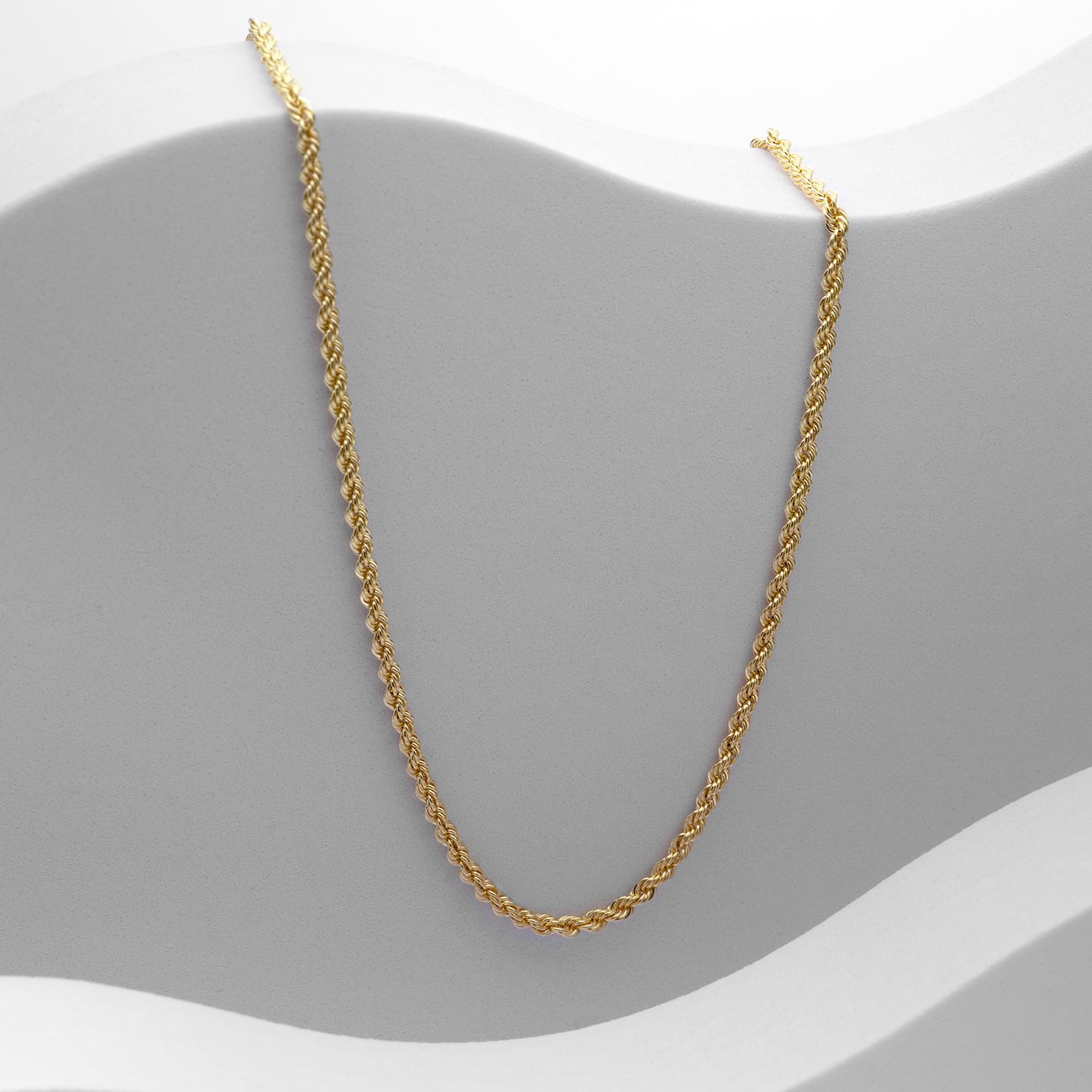 CHRIST collier: Een gouden CHRIST collier van 585 geelgoud ligt op een lichtgrijze, golvende ondergrond.