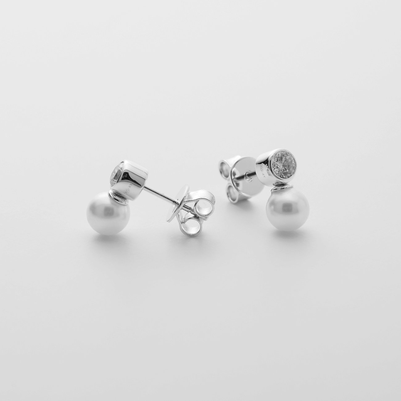 Zwei JETTE Ohrstecker aus recyceltem 925er Silber mit runden Perlen und klaren Schmucksteinen.