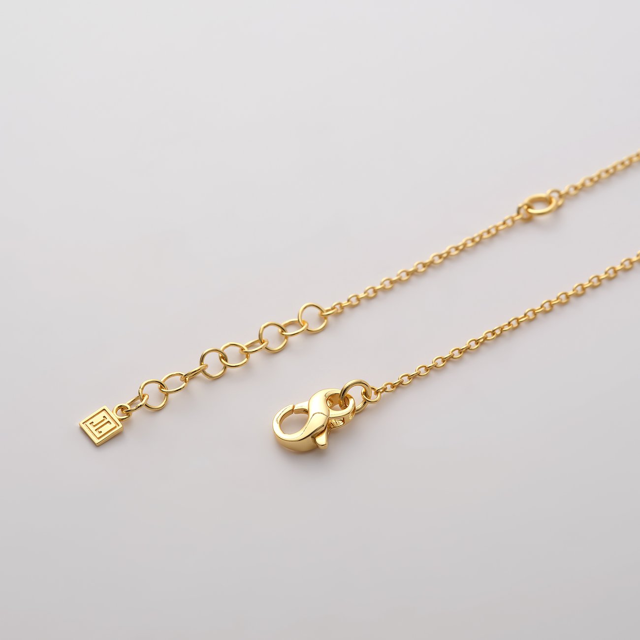 Nahaufnahme der goldenen Verlängerungskette mit Karabinerverschluss und quadratischem JETTE Markenanhänger aus recyceltem Silber.