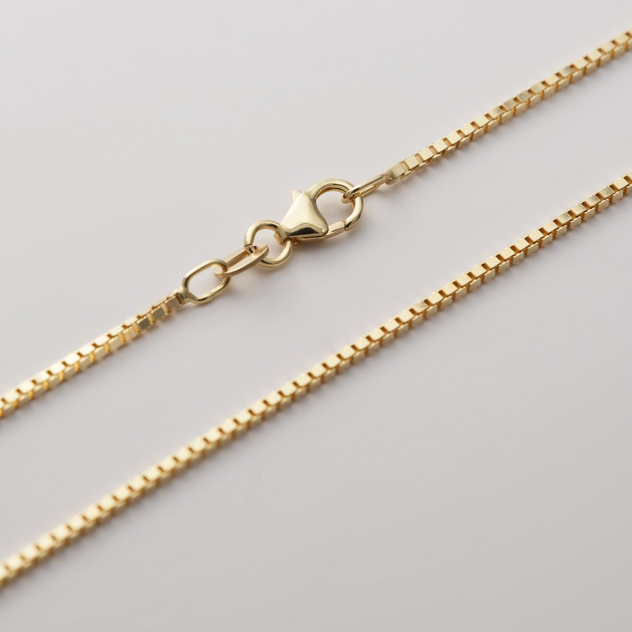 CHRIST Kettenanhänger aus glänzendem 375er Gelbgold, liegend präsentiert mit sichtbarem Karabinerverschluss.
