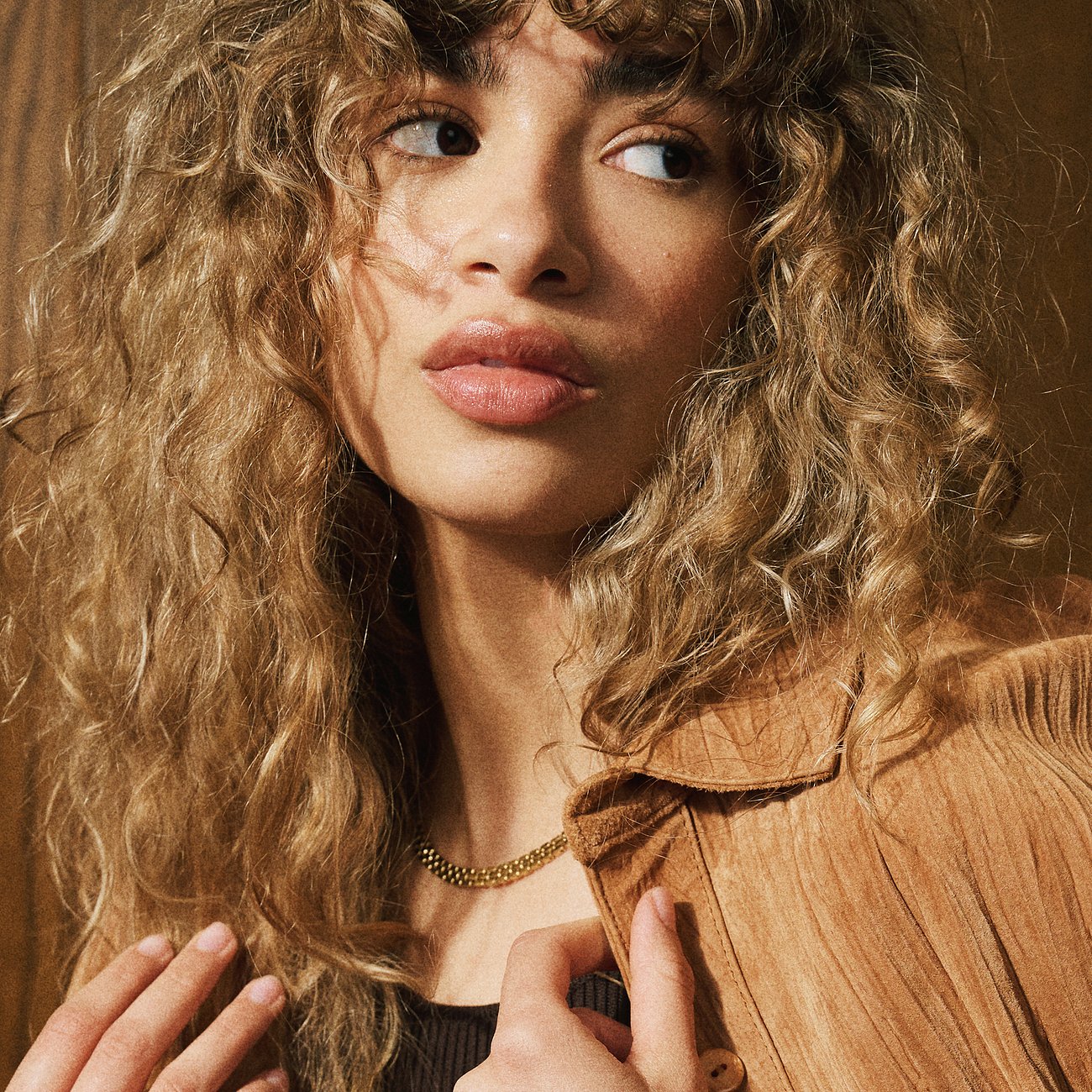 Eine Frau trägt ein Fossil Halsschmuck aus goldfarbenem Edelstahl, ihre Hände berühren die Jacke.