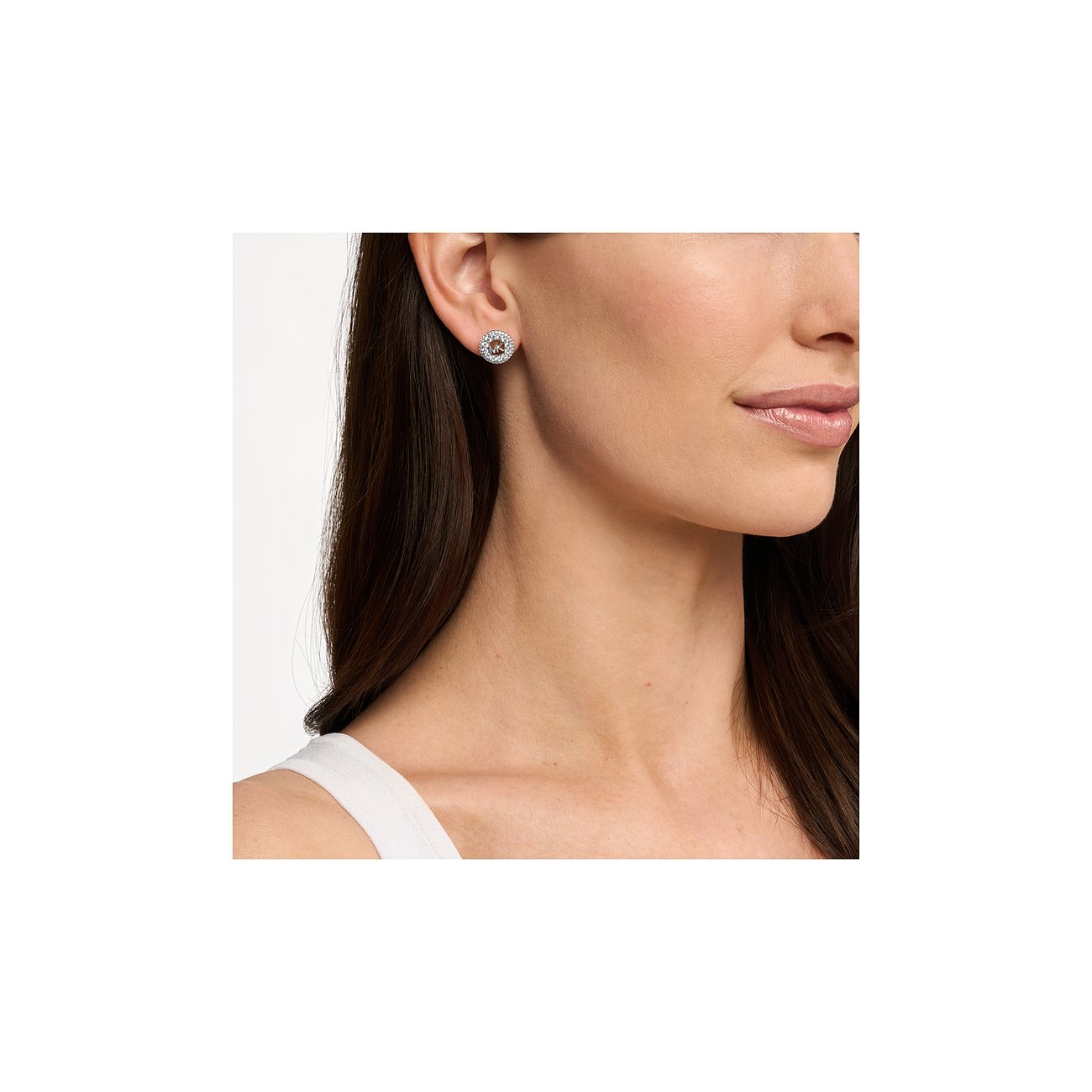 Sull'orecchio di una donna è appoggiato un orecchino rotondo Michael Kors in argento con zirconi color oro rosa.