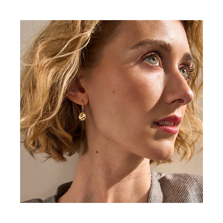 Gros plan d'une femme portant une boucle d'oreille Skagen dorée en acier inoxydable avec cercle texturé.