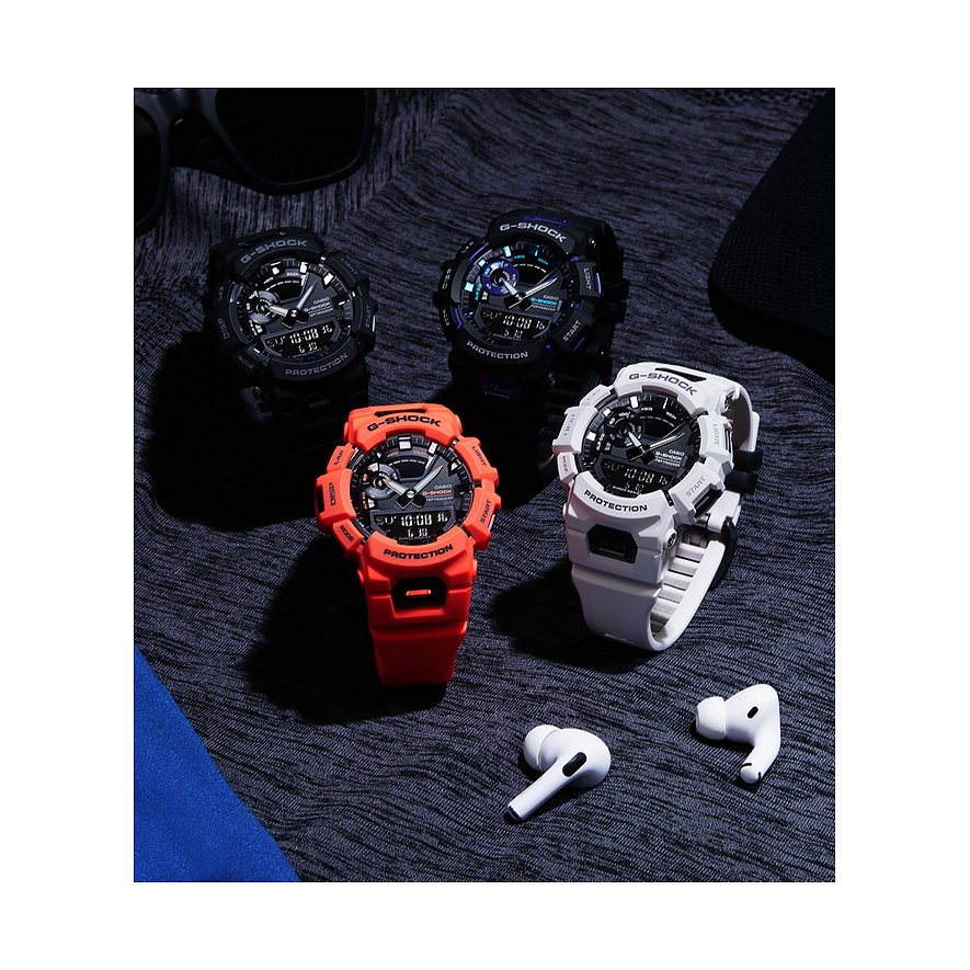 Eine Nahaufnahme von vier Casio Herrenuhren aus Resin in Schwarz, Lila, Orange und Weiß auf dunklem Stoff.