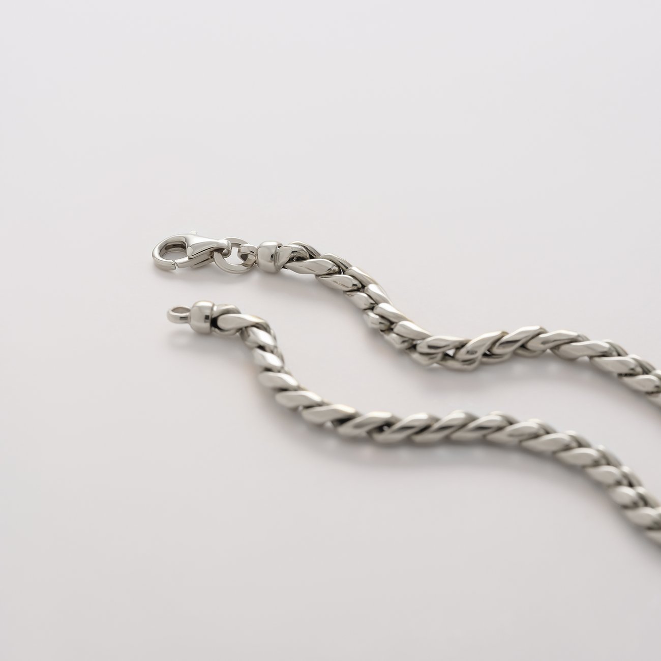 Nahaufnahme einer CHRIST Halskette aus 585er Weißgold, elegant geschlängelt auf glatter Fläche, zeigt Karabinerverschluss.