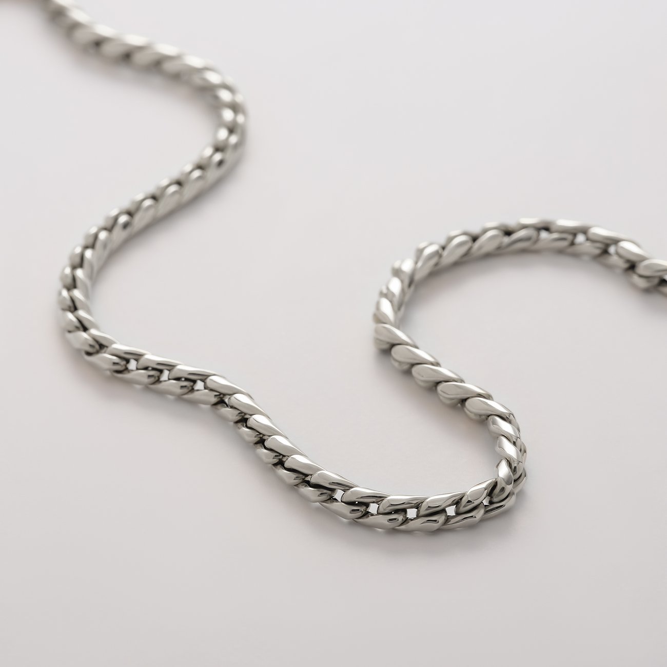 Nahaufnahme einer flachen, glänzenden CHRIST Curb-Kette aus 585er Weißgold, elegant geschwungen, auf hellem Hintergrund.