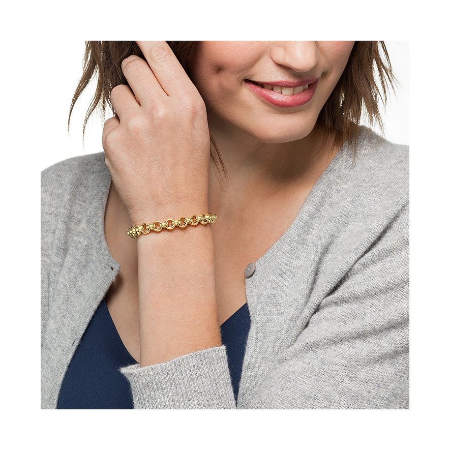 Een CHRIST 585 geelgouden armband is te zien aan de pols van een lachende vrouw, die haar haar aanraakt.