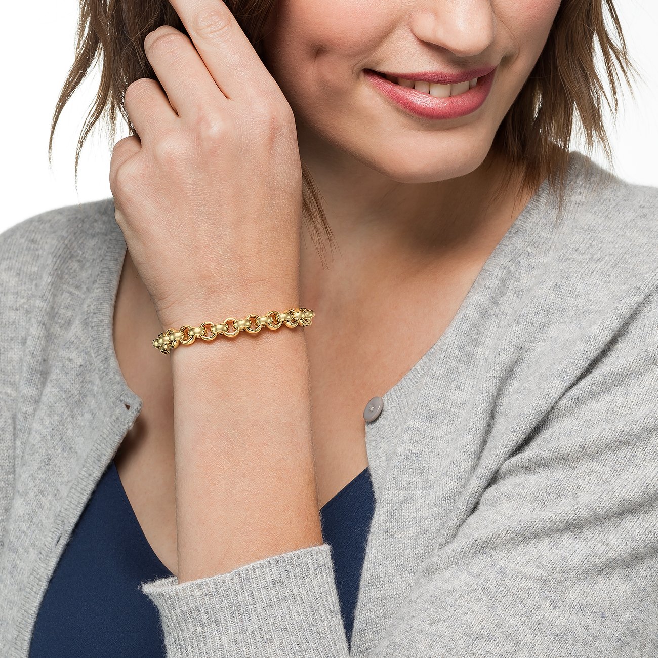 Een CHRIST 585 geelgouden armband is te zien aan de pols van een lachende vrouw, die haar haar aanraakt.