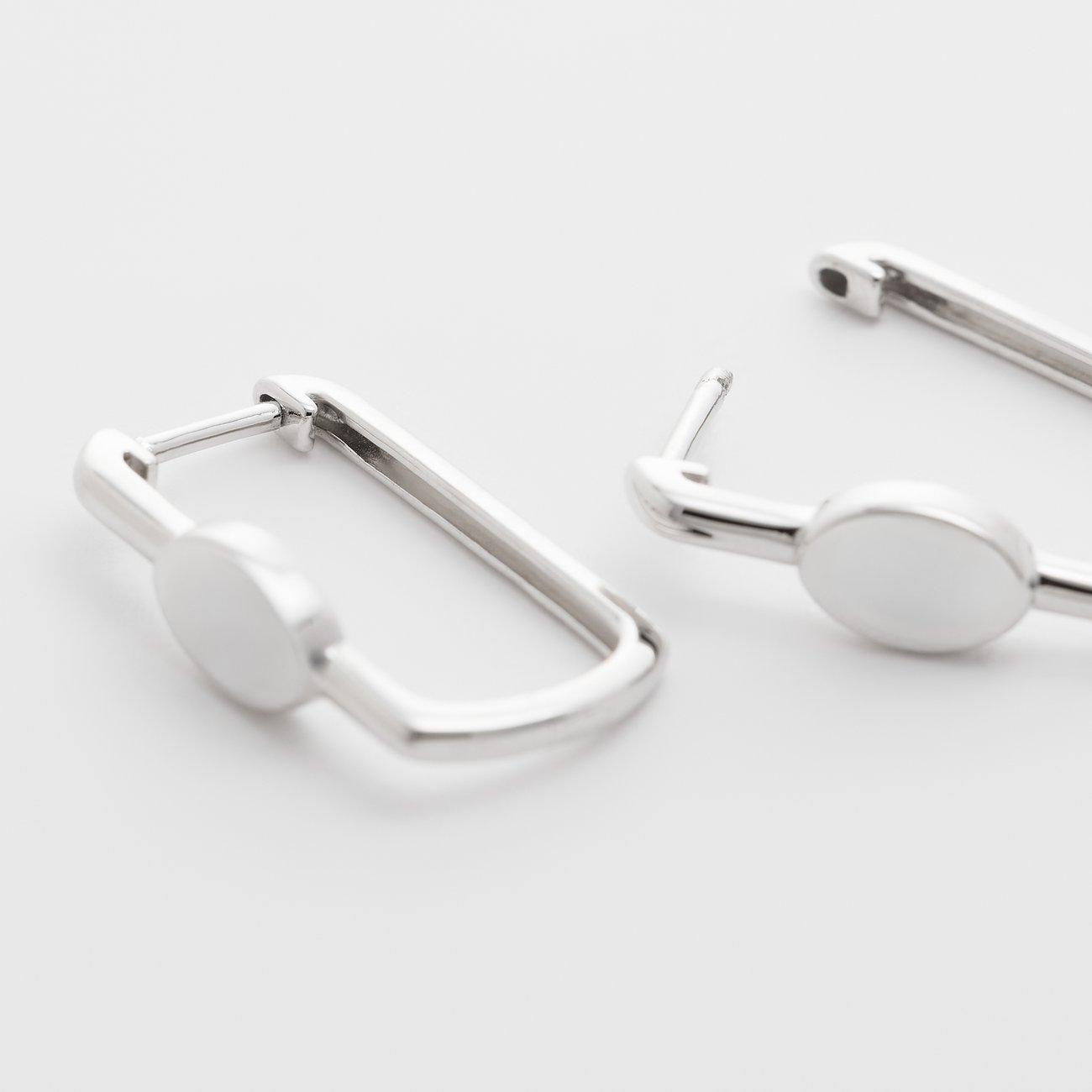 Närbild av två glänsande FAVS örhängen i 925 silver med fyrkantiga fästen och ovala detaljer.