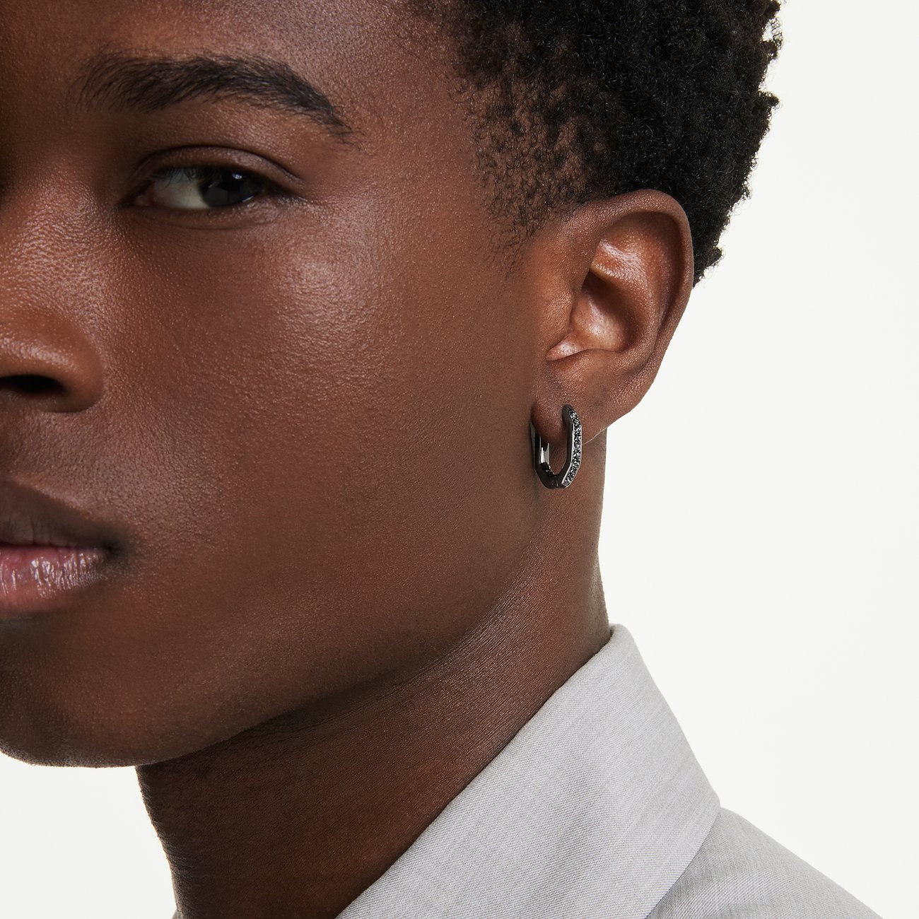 Nahaufnahme: Gesicht einer Person mit einem einzelnen schwarzen Swarovski Ohrring aus Metall mit funkelnden Farbedelsteinen.