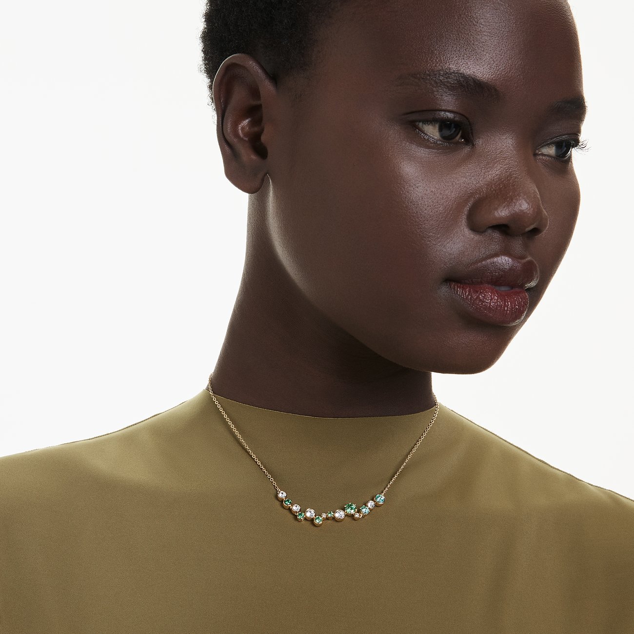 Eine Frau trägt eine Swarovski Halskette aus Metall mit bunten Swarovski-Kristallen in Grün und Weiß.