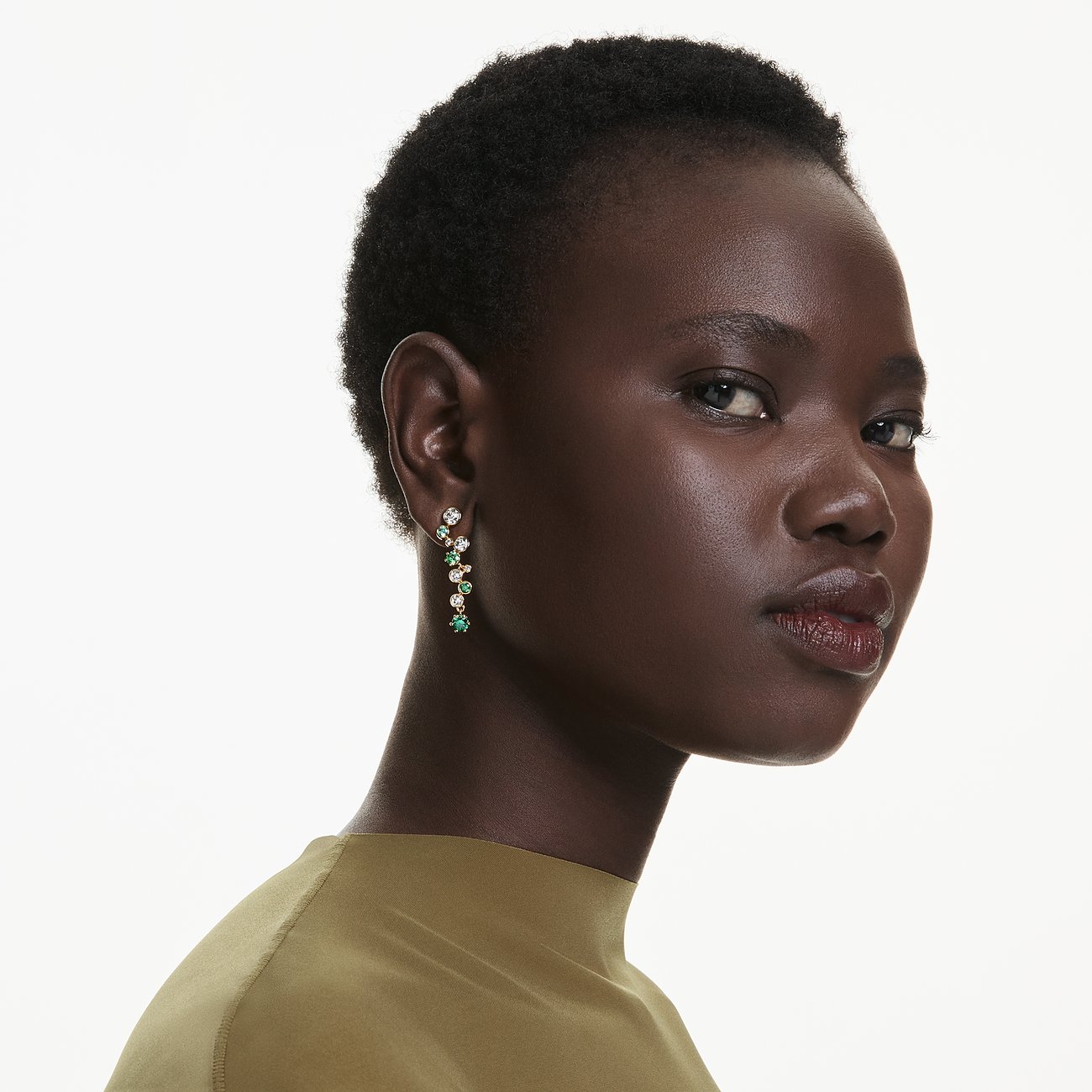 Een model draagt   Swarovski oorbellen van metaal met groene en witte Swarovski kristallen.