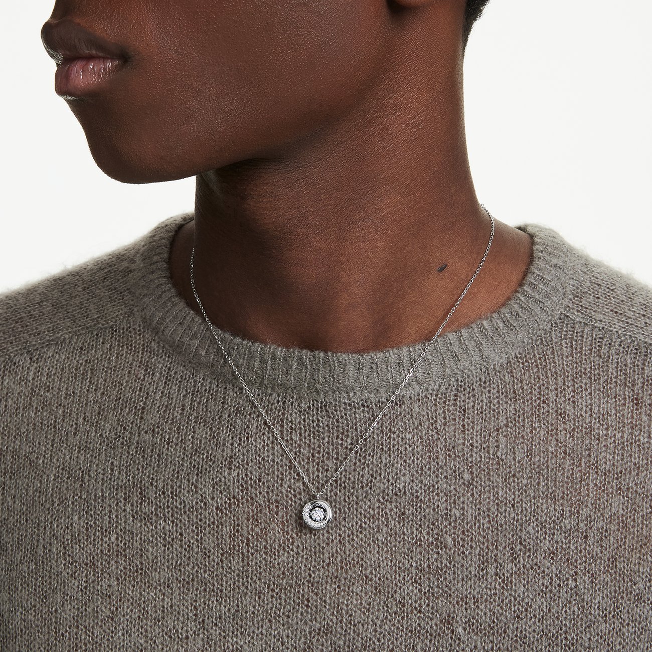 Een paspop draagt een korte metalen Swarovski-halsketting met een ronde, decoratieve hanger.
