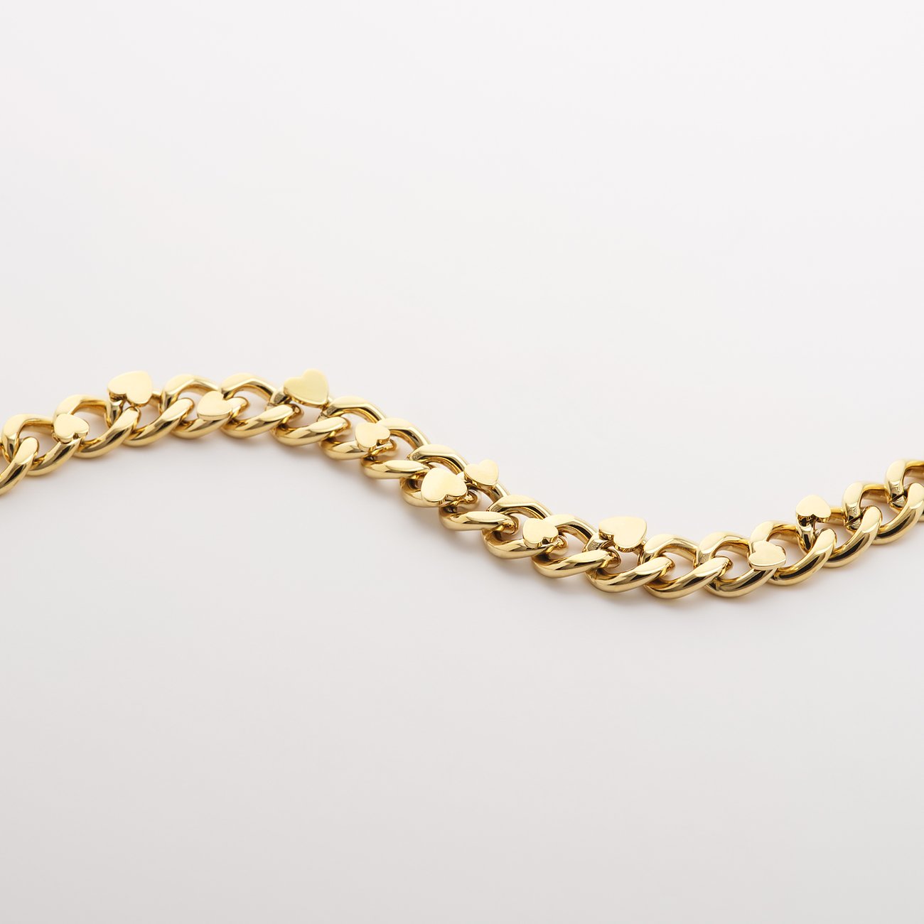 Nærbillede af en gylden Guido Maria Kretschmer halskæde i rustfrit stål, der ligger i bløde bølger.