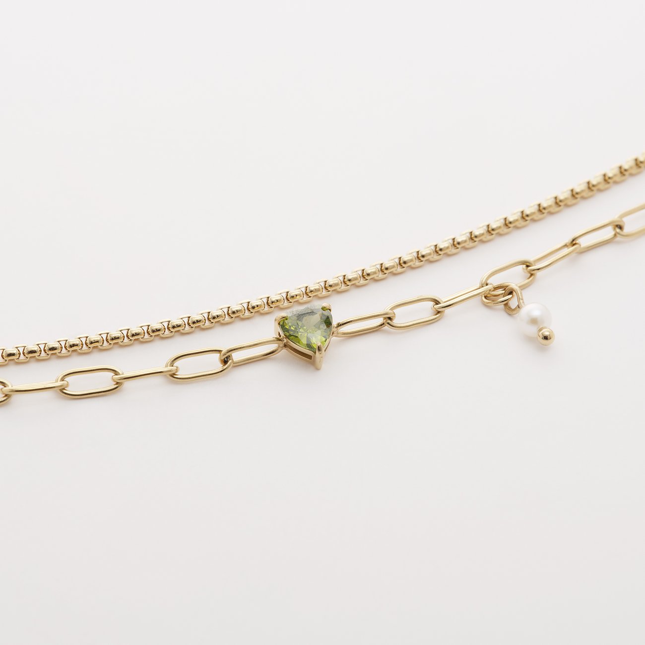 Ein Guido Maria Kretschmer goldenes Edelstahl-Armband mit zwei Ketten, einem herzförmigen grünen Zirkonia und einer Perle.