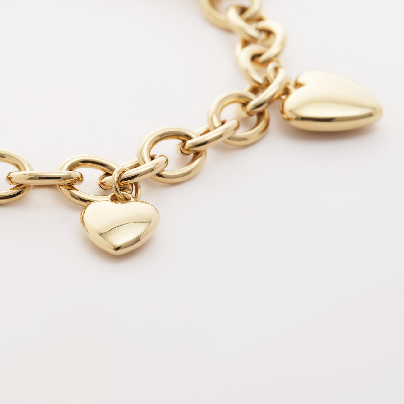 Ein goldenes Guido Maria Kretschmer Edelstahl-Armband mit herzförmigen Anhängern auf weißem Hintergrund.