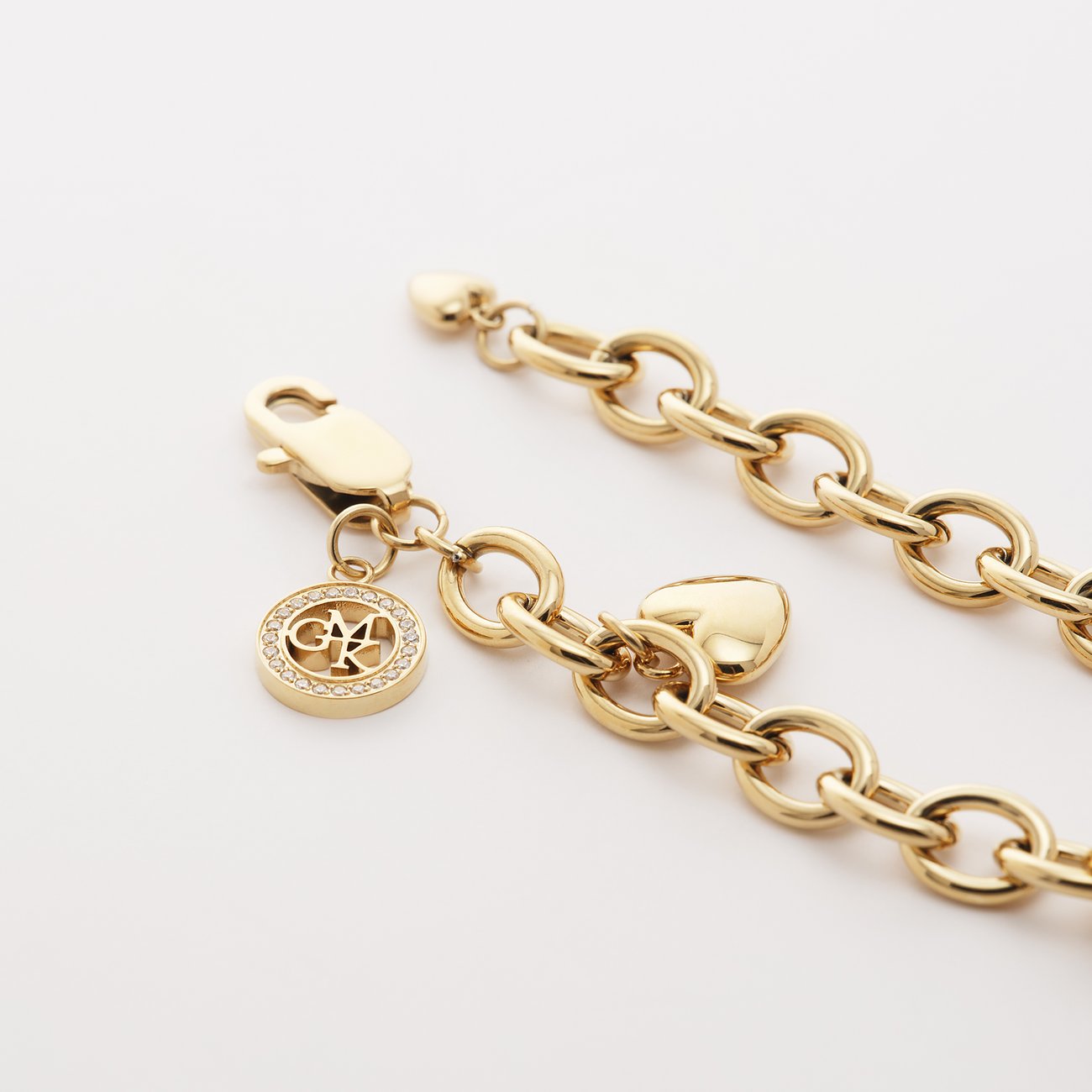 Close-up eines Guido Maria Kretschmer Edelstahl-Armbands in Gold von oben mit Herzanhänger und rundem Marken-Charm.