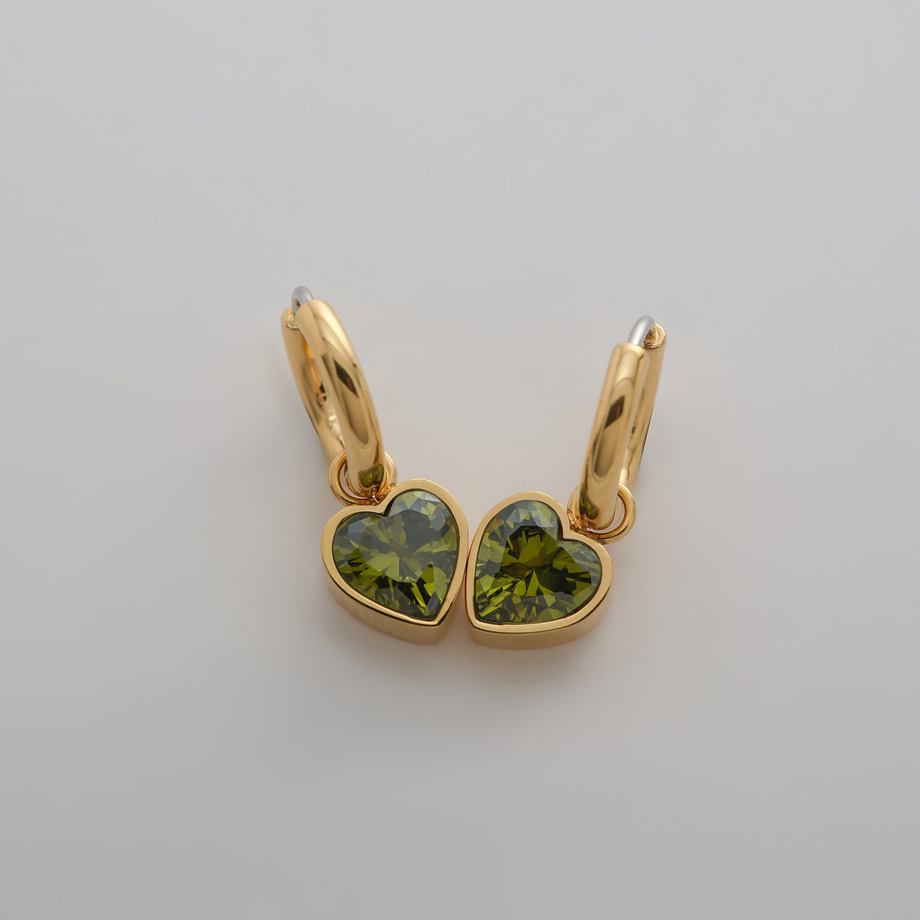 Guido Maria Kretschmer Ohrschmuck aus goldfarbenem Edelstahl mit herzförmigen, grünen Zirkonia-Farbsteinen.