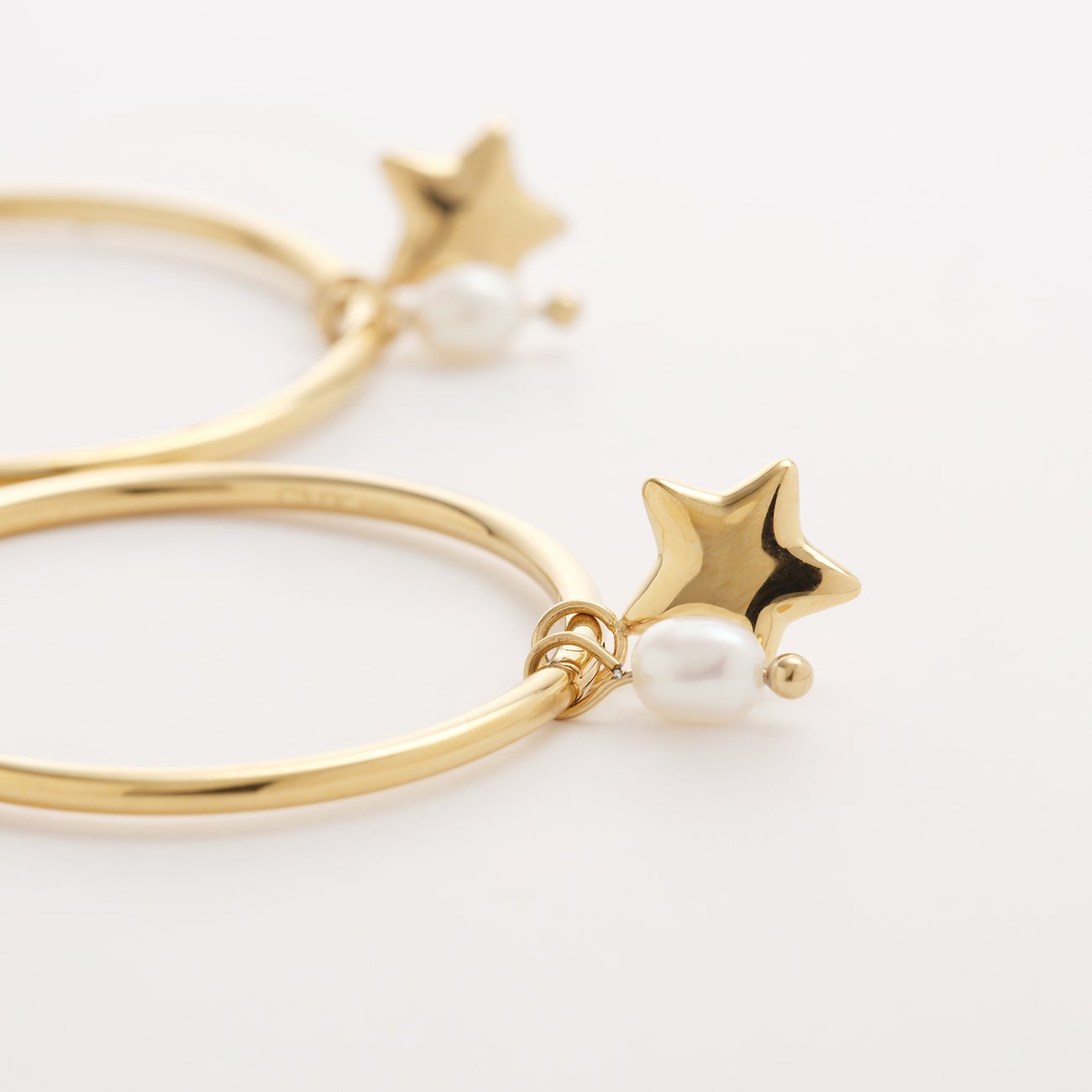 En Guido Maria Kretschmer ørering i guldfarvet rustfrit stål med stjernevedhæng og perle.