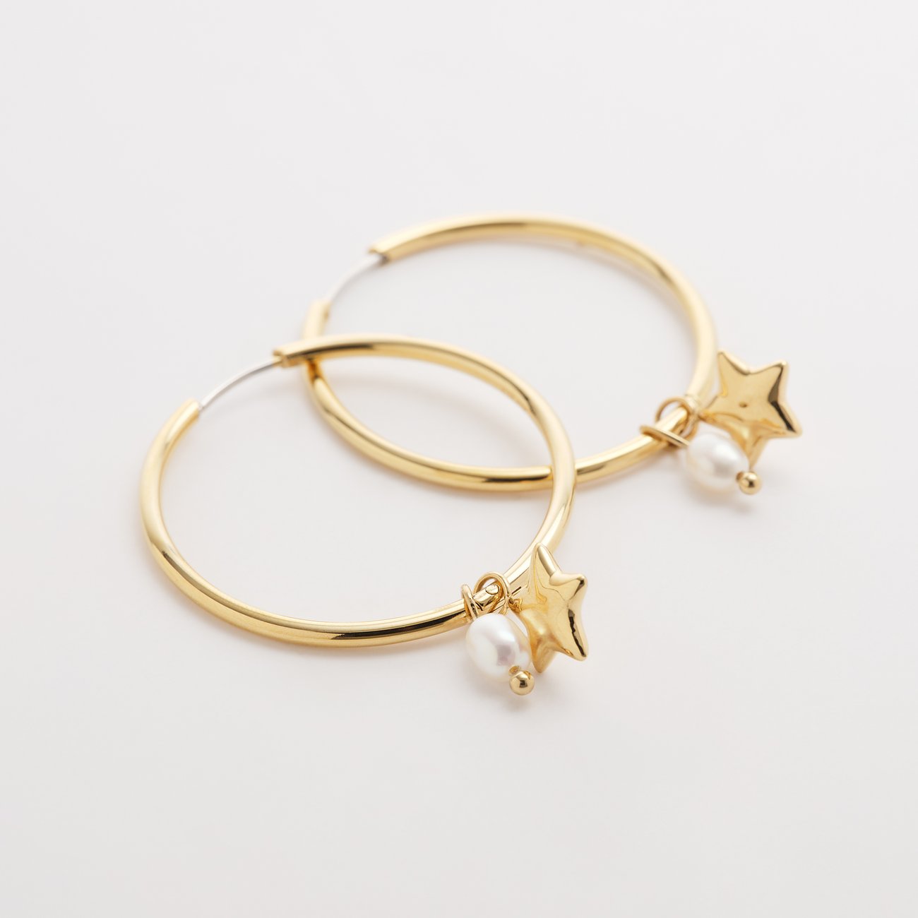 Et par guldfarvede Guido Maria Kretschmer øreringe af rustfrit stål med stjerne- og perlependler.