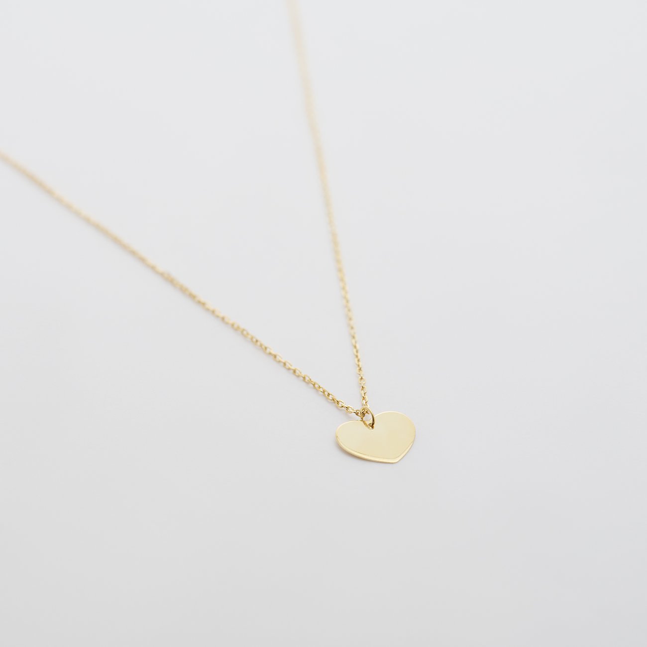 FAVS Halsschmuck: Zarte Gelbgoldkette mit glänzendem Herz-Plättchen, schwebend über weissem Hintergrund.