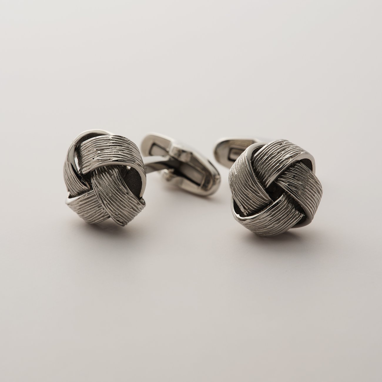 FAVS Manschettenknöpfe aus Edelstahl, Vorderansicht, knotenförmig mit feinen, parallelen Rillen in Silberoptik.