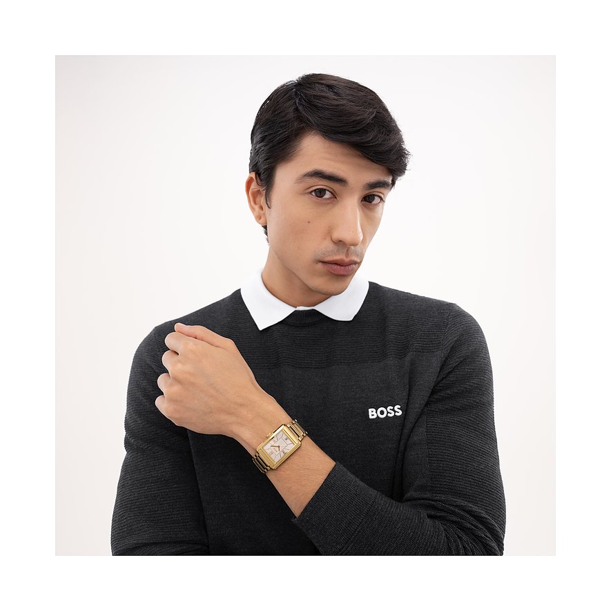 Nahaufnahme eines Mannes, der eine goldfarbene Herrenuhr aus Edelstahl von Boss mit rechteckigem Zifferblatt trägt.