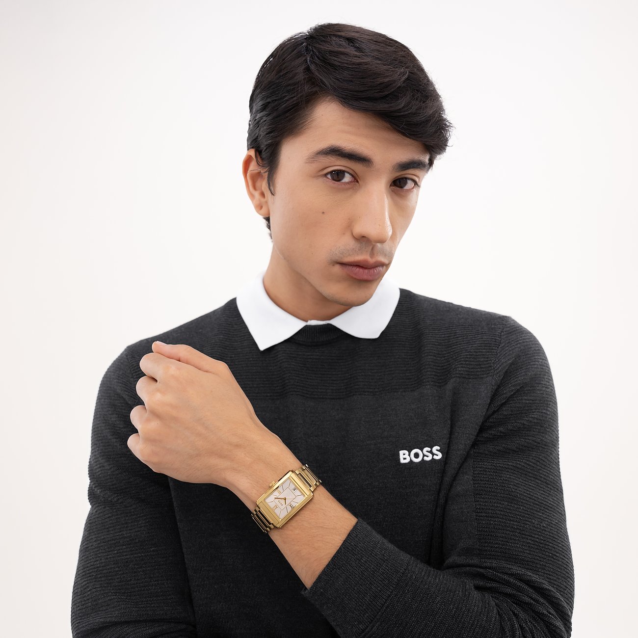 Nahaufnahme eines Mannes, der eine goldfarbene Herrenuhr aus Edelstahl von Boss mit rechteckigem Zifferblatt trägt.