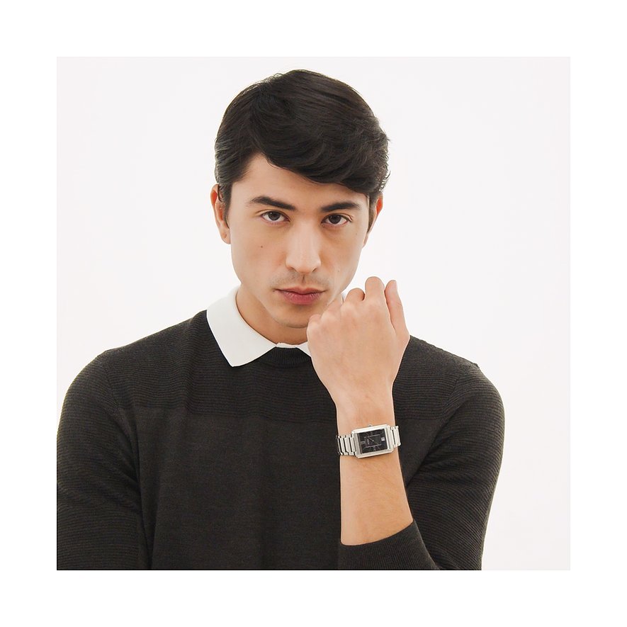 Ein junger Mann mit dunklen Haaren trägt eine Boss Herrenuhr aus silberfarbenem Edelstahl mit schwarzem Zifferblatt.