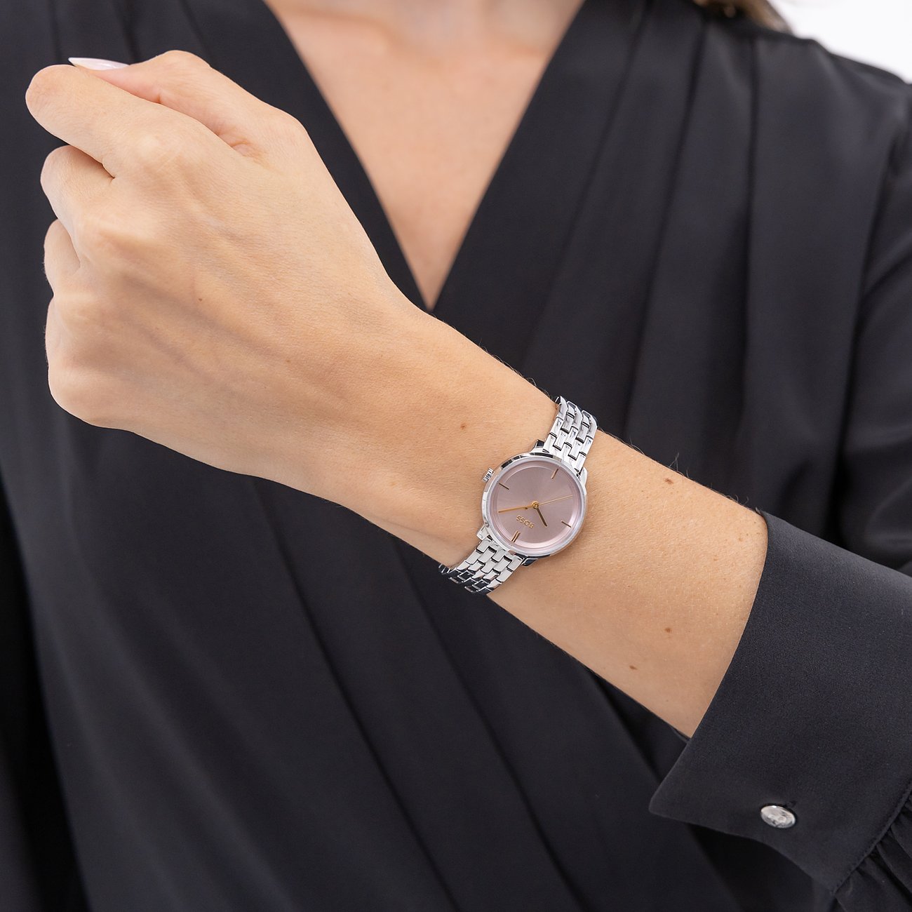 Am Handgelenk einer Frau ist eine Boss Damenuhr aus Edelstahl mit einem roséfarbenen Zifferblatt zu sehen.
