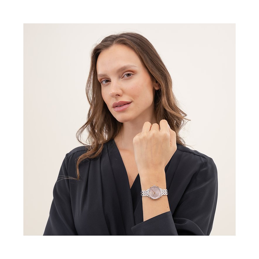Eine Frau trägt die Boss Damenuhr aus Edelstahl mit rosafarbenem Zifferblatt am Handgelenk und blickt in die Kamera.