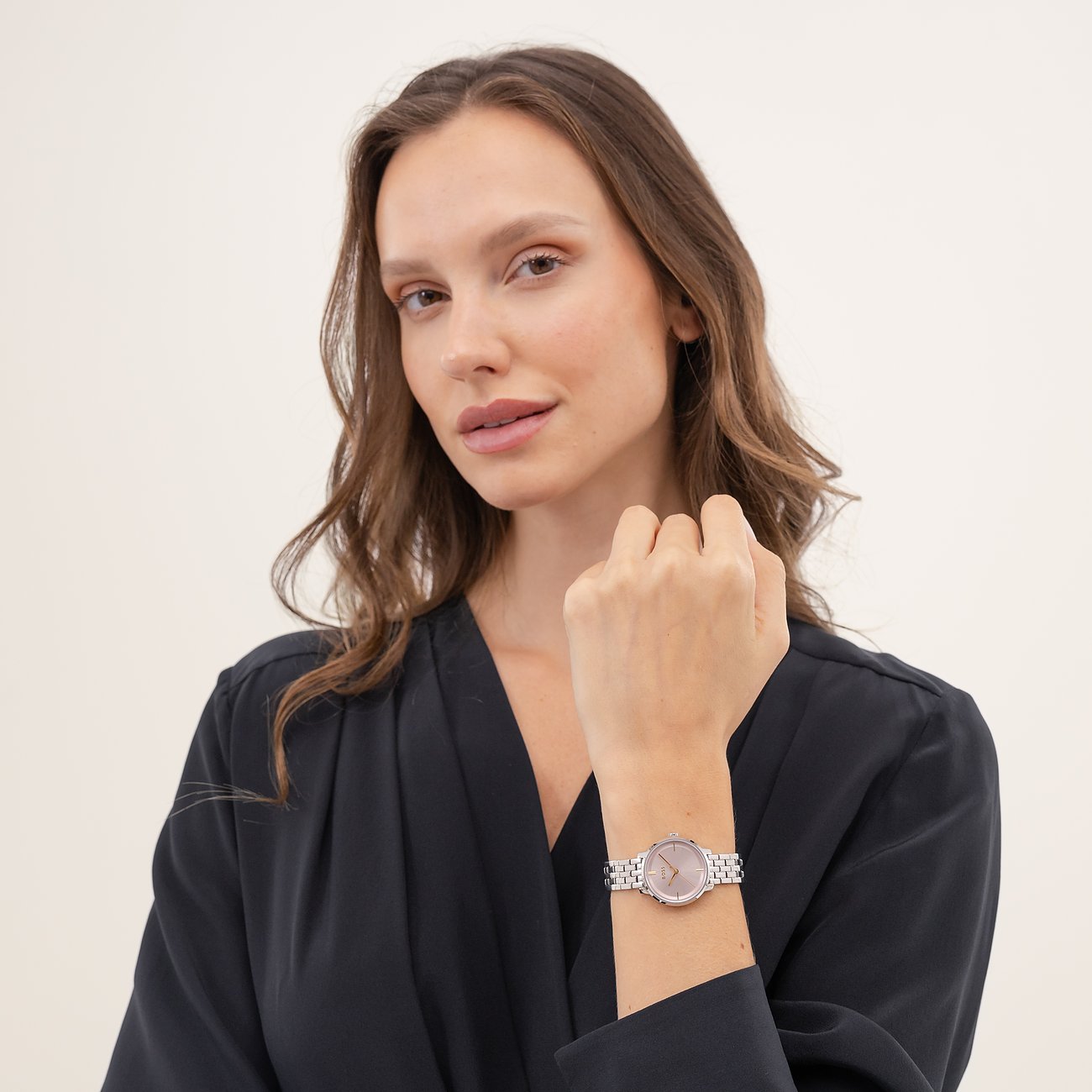 Eine Frau trägt die Boss Damenuhr aus Edelstahl mit rosafarbenem Zifferblatt am Handgelenk und blickt in die Kamera.