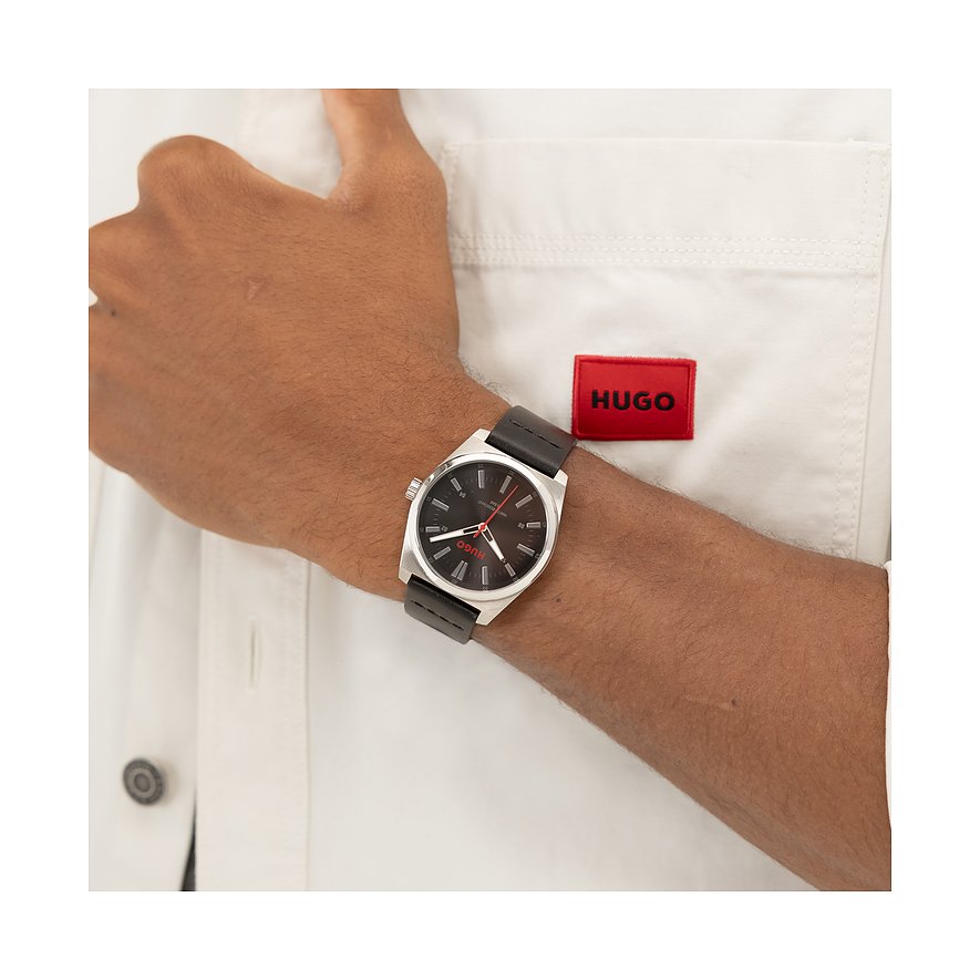 Am Handgelenk eines Mannes getragene Hugo Herrenuhr aus silberfarbenem Edelstahl mit schwarzem Lederarmband und Zifferblatt.
