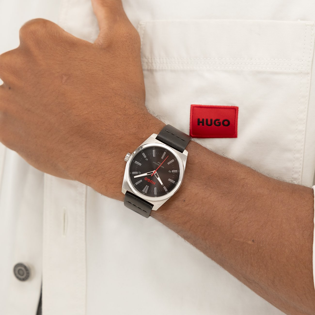 Am Handgelenk eines Mannes getragene Hugo Herrenuhr aus silberfarbenem Edelstahl mit schwarzem Lederarmband und Zifferblatt.