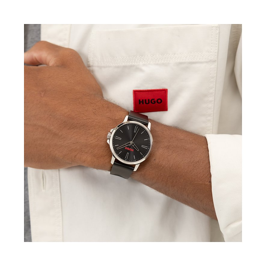 Am Handgelenk getragene Hugo Herrenuhr aus Edelstahl mit dunklem Zifferblatt, roten Akzenten und schwarzem Lederarmband.