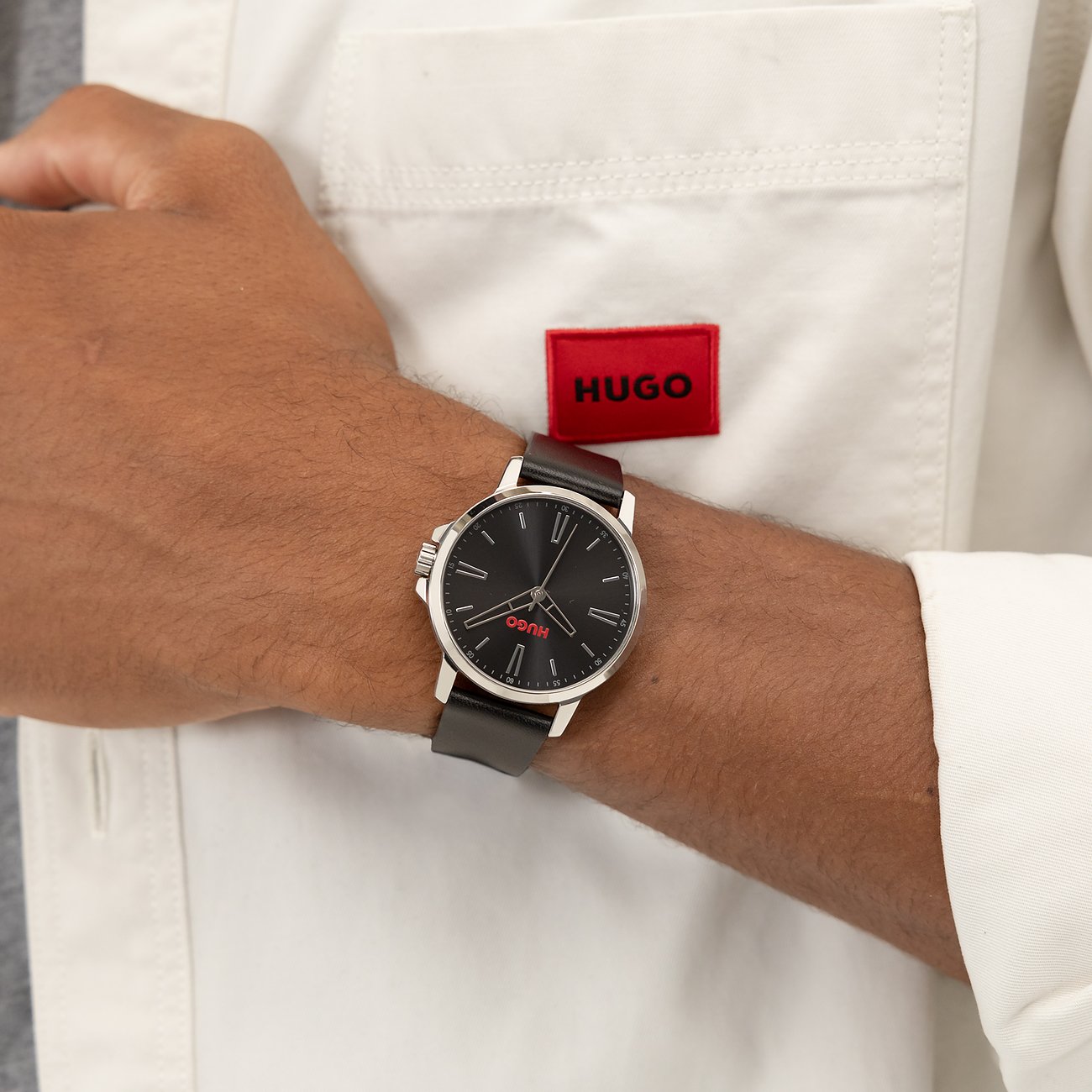 Am Handgelenk getragene Hugo Herrenuhr aus Edelstahl mit dunklem Zifferblatt, roten Akzenten und schwarzem Lederarmband.