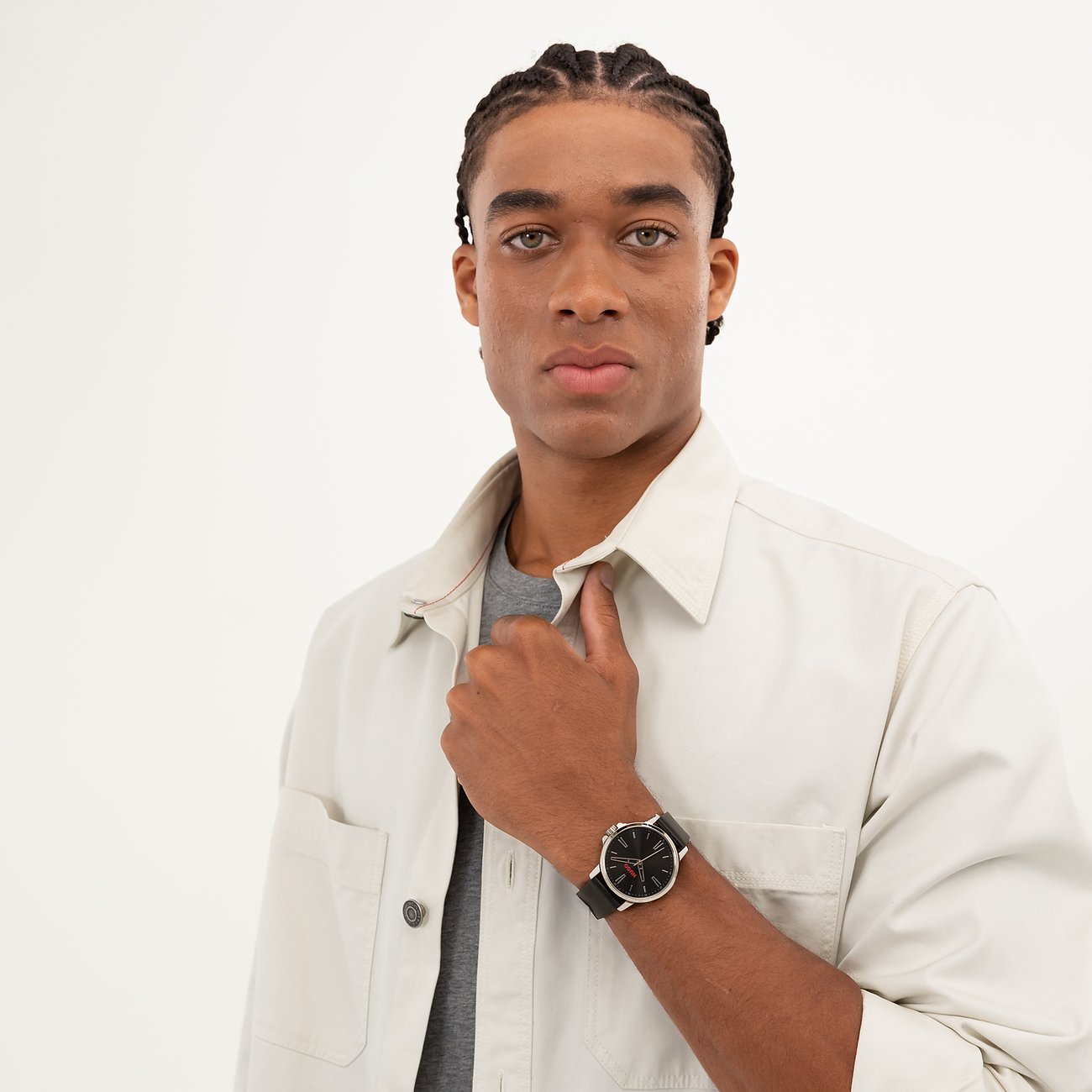 Ein Mann mit geflochtenen Haaren und einem beigen Hemd posiert mit dem Hugo Herrenuhren-Modell aus Edelstahl am Handgelenk.