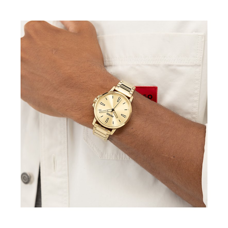 Gouden Hugo herenhorloge van roestvrij staal, aan de pols gedragen, met ronde wijzerplaat en gouden band.