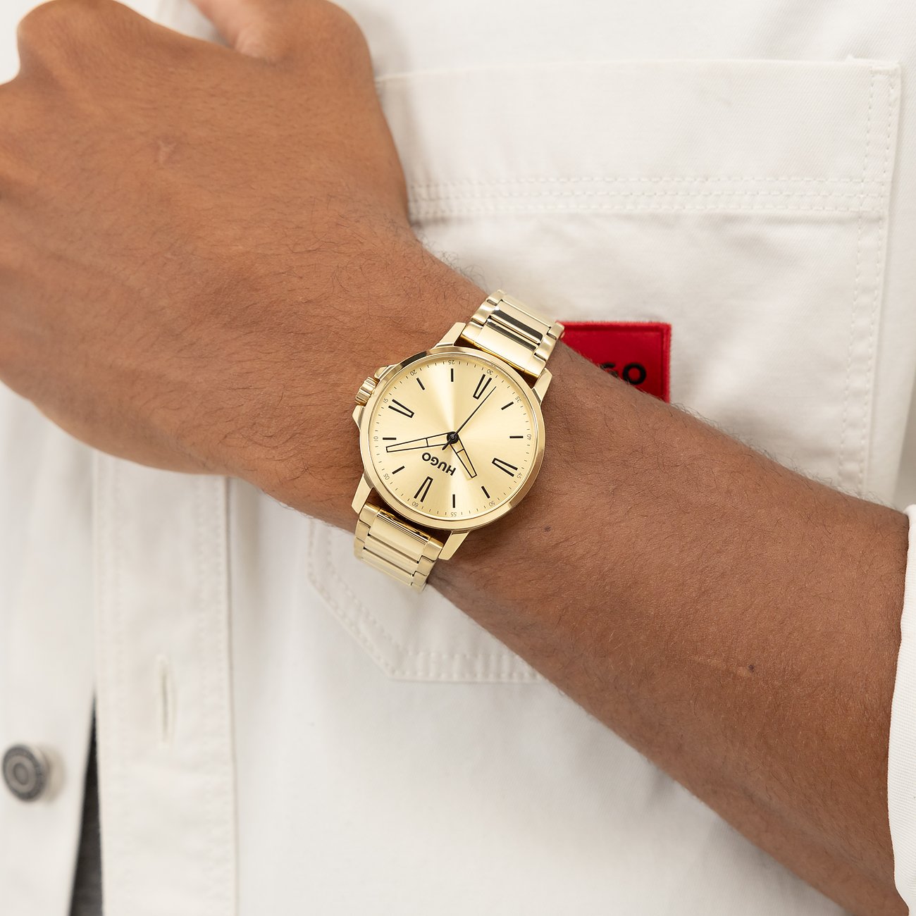 Gouden Hugo herenhorloge van roestvrij staal, aan de pols gedragen, met ronde wijzerplaat en gouden band.