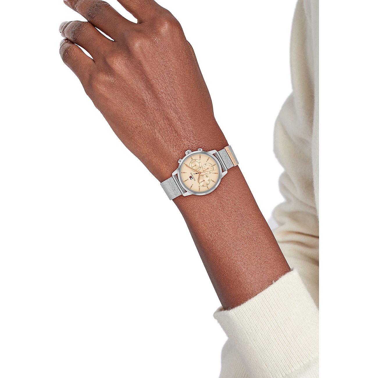 Close-up van iemands arm met een Tommy Hilfiger dameshorloge van roestvrij staal met een lichte wijzerplaat.