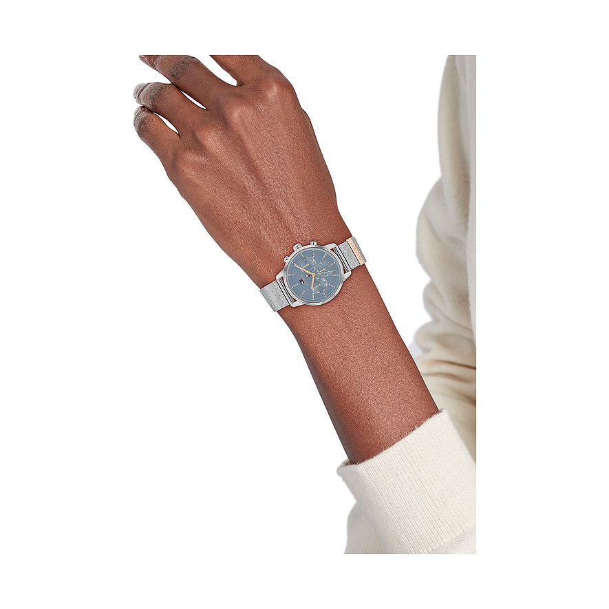 Tommy Hilfiger Damenuhr aus Edelstahl mit blauem Zifferblatt und silberfarbenem Milanaise-Armband am Handgelenk einer Frau.