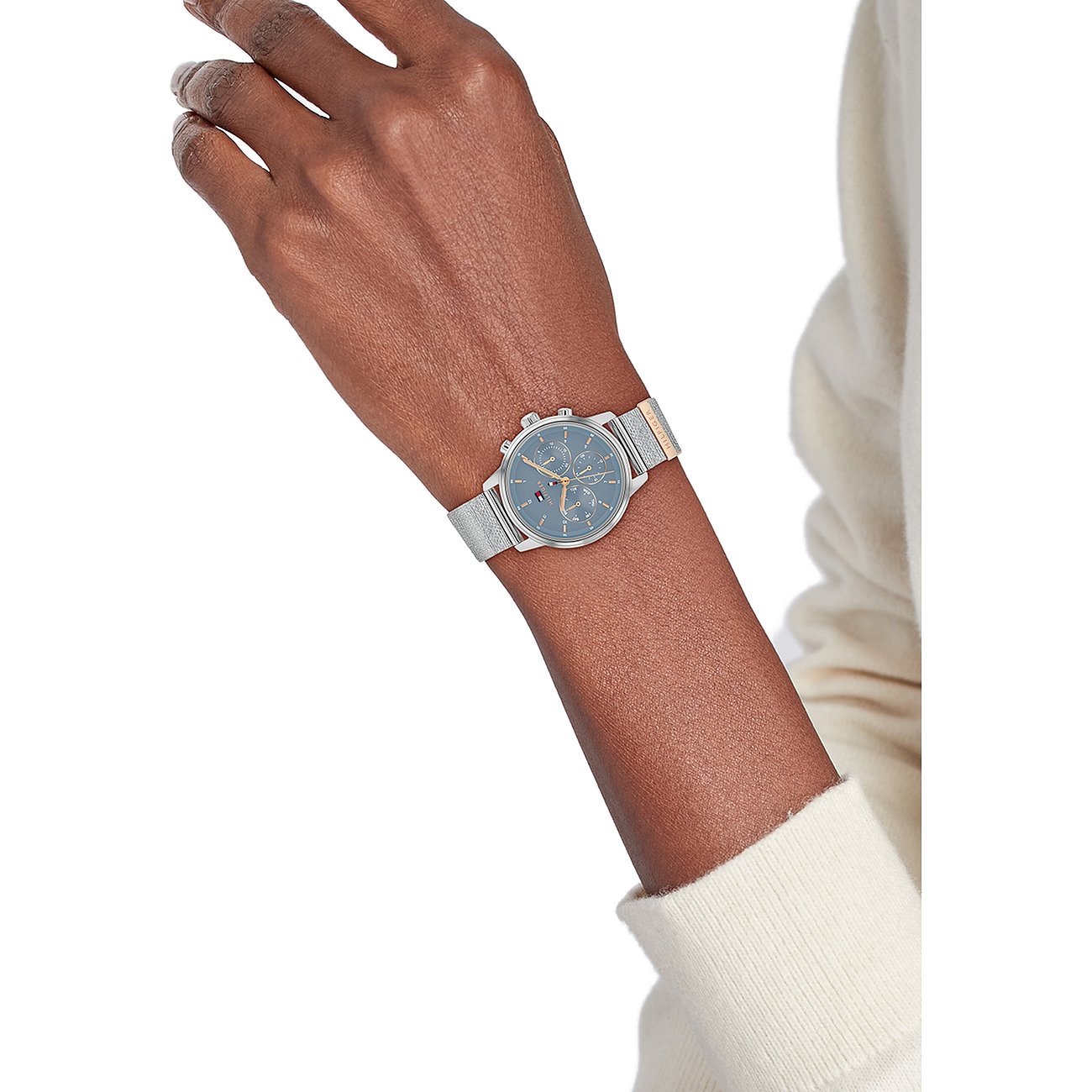 Tommy Hilfiger Damenuhr aus Edelstahl mit blauem Zifferblatt und silberfarbenem Milanaise-Armband am Handgelenk einer Frau.