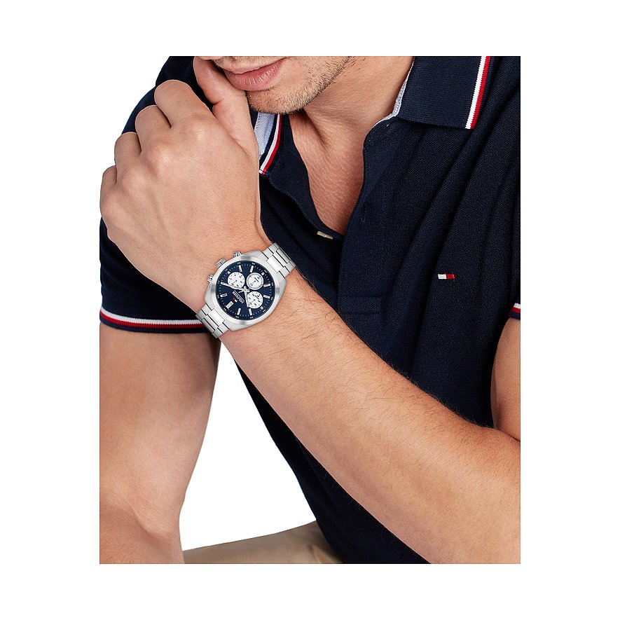 Ein Mann trägt eine Tommy Hilfiger Herrenuhr aus Edelstahl mit blauem Ziffernblatt an seinem linken Handgelenk.