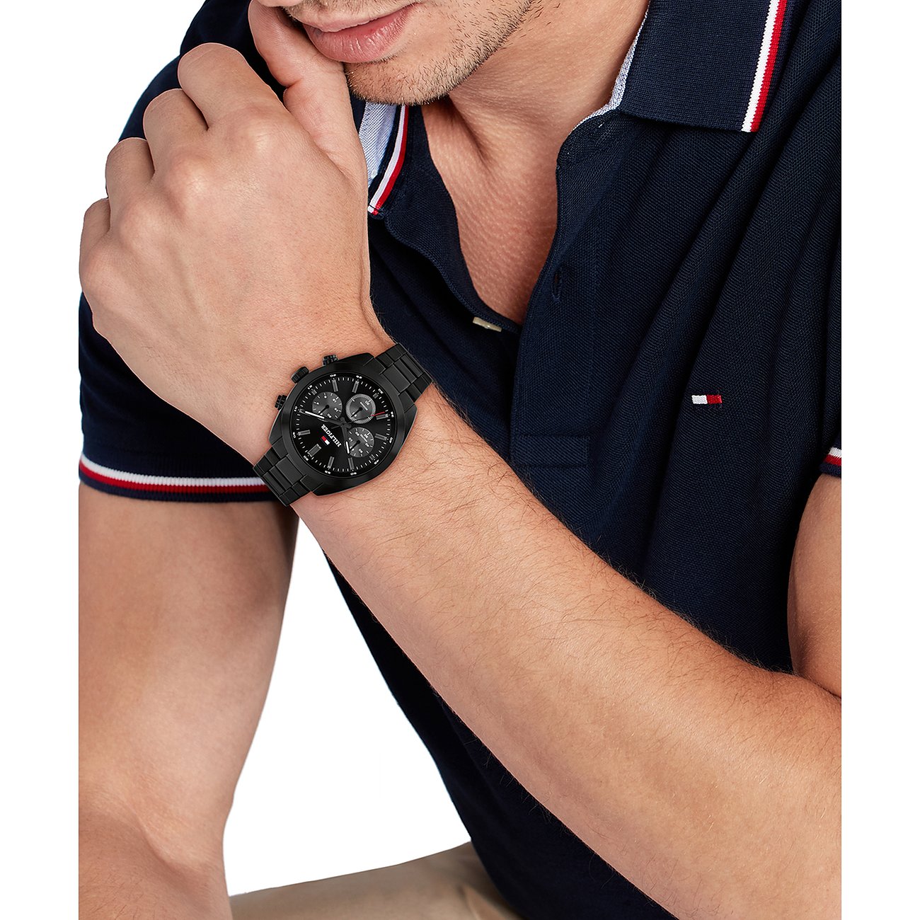 Een man in een poloshirt draagt het Tommy Hilfiger herenhorloge van zwart roestvrij staal om zijn pols.