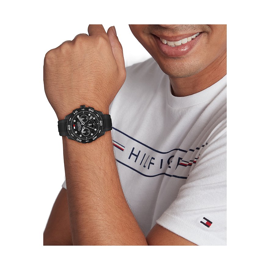 Nahaufnahme einer schwarzen Tommy Hilfiger Herrenuhr aus Edelstahl und Aluminium am Handgelenk eines Mannes.