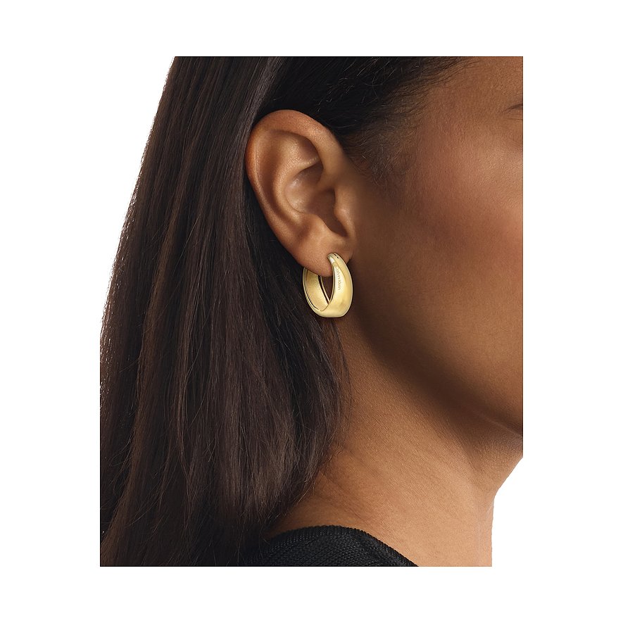 Am Ohr getragenes goldfarbenes Calvin Klein Ohrschmuck Creolen-Ohrring aus Edelstahl, von der Seite fotografiert.