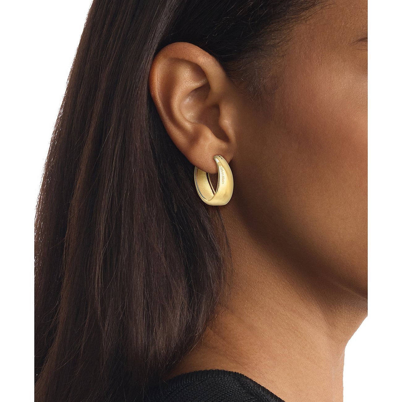 Am Ohr getragenes goldfarbenes Calvin Klein Ohrschmuck Creolen-Ohrring aus Edelstahl, von der Seite fotografiert.