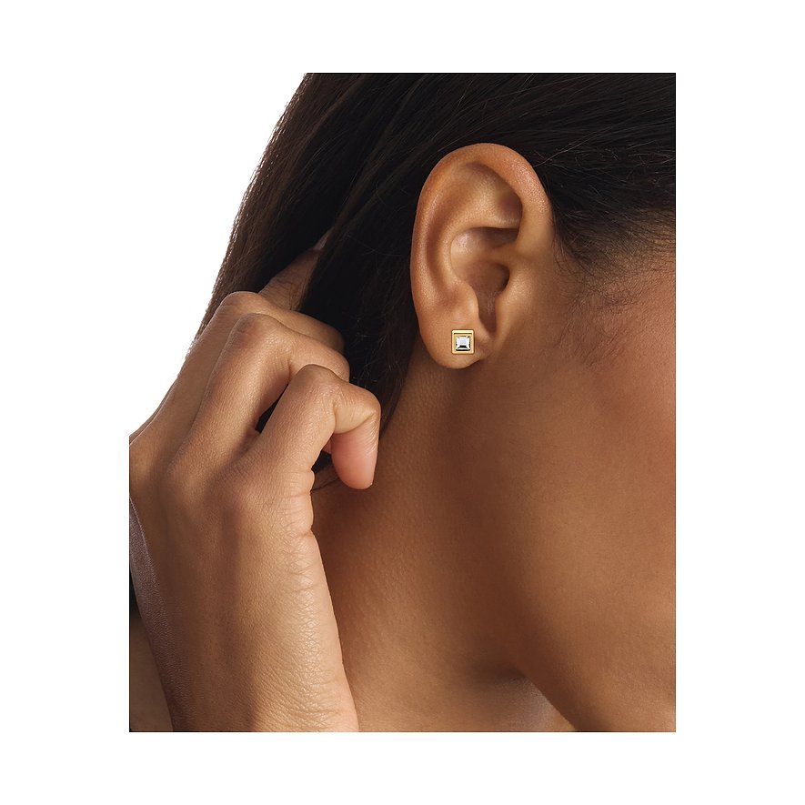 Ein Calvin Klein Ohrstecker aus goldfarbenem Edelstahl mit einem quadratischen, klaren Schmuckstein am Ohr eines Models.
