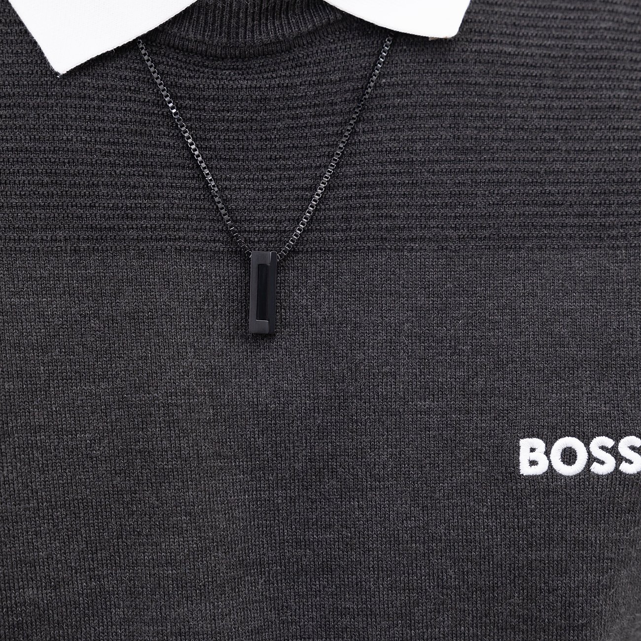 Boss ketting van zwart roestvrij staal met rechthoekige hanger, gedragen over een zwarte trui.